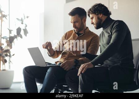 Fokussierte Mitarbeiter des Unternehmens, die auf den Laptop-Bildschirm schauen und gemeinsam an Geschäftungsprojekten in modernen Büros und auf freiem Raum arbeiten Stockfoto