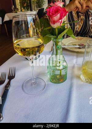 Ein Glas Weißwein mit einer rosa Rose auf einem Tisch in einem Bistro-Restaurant Stockfoto