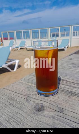 Köstlicher, kühler Eistee ohne Marke mit Zitrone und Eiswürfel auf einem Terrassentisch am warmen Strand Stockfoto