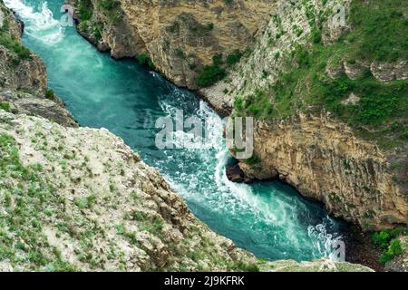 Blick von oben auf einen schnellen Gebirgsfluss, der am Fuße eines tiefen Canyons fließt Stockfoto