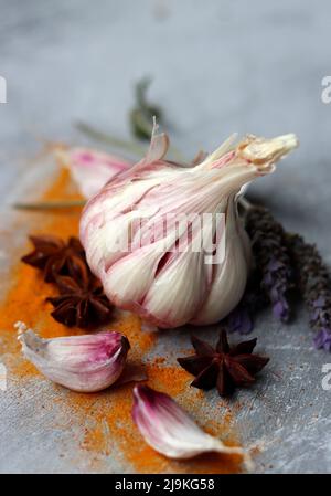 Gewürze auf einem Tisch. Nahaufnahme von Knoblauchzehen und Knoblauchzehen, Kurkuma-Pulver, Rosmarin, Anis und Lavendel. Hellgrauer Hintergrund. Stockfoto