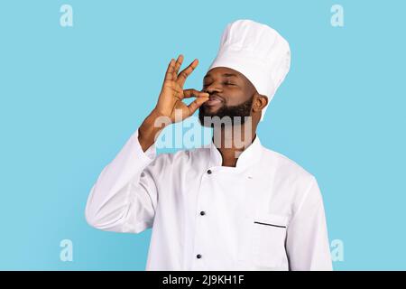 Schöner Schwarzer Männlicher Koch In Uniform Küssende Finger, Über Blauem Hintergrund Stehend Stockfoto