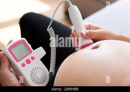 Eine Schwangerin mit einem fetalen doppler hört dem Baby zu Hause auf dem Sofa zu Stockfoto