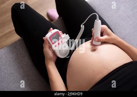 Eine Schwangerin mit einem fetalen doppler hört dem Baby zu Hause auf dem Sofa zu Stockfoto