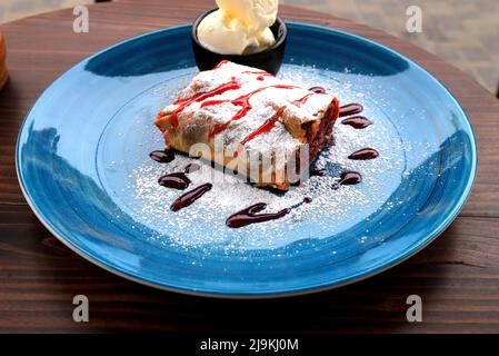 Wiener Obststrudel und Eis auf blauem Teller im Café, Restaurant. Heißer, köstlicher Dessertstrudel, süßes Blätterteig in Österreich Stockfoto