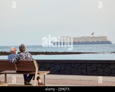 Ein älteres Paar, das von hinten auf einer Bank mit Blick auf das Meer mit einem Kreuzschiff gesehen wird Stockfoto