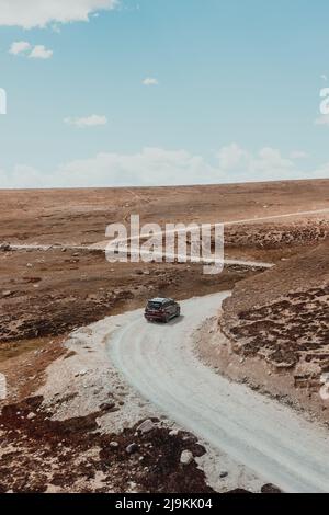 Geländewagen, der an einem Sommertag durch eine windige, unbefestigte Straße durch die Hügel des Deosai-Nationalparks fährt Stockfoto