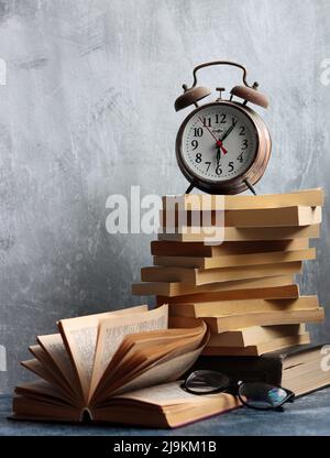 Stapel alter Bücher, Vintage-Uhr auf einem Schreibtisch. Hellgrauer strukturierter Hintergrund mit Kopierbereich. Bildungskonzept. Stockfoto