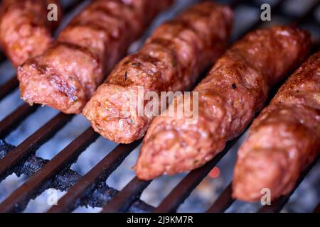 Preparing meat rolls called mici or mititei on barbecue. close up of grill with burning fire with flame and smoke. Stock Photo