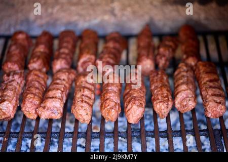 Preparing meat rolls called mici or mititei on barbecue. close up of grill with burning fire with flame and smoke. Stock Photo