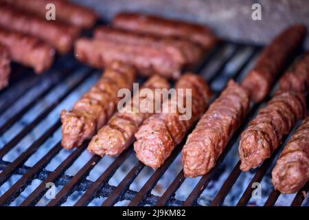 Preparing meat rolls called mici or mititei on barbecue. close up of grill with burning fire with flame and smoke. Stock Photo