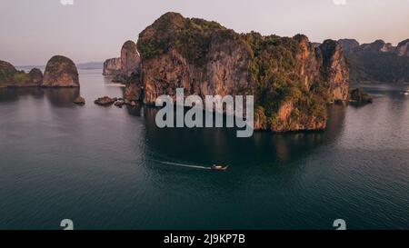 Sonnenaufgang am Railay Beach in Krabi Thailand mit einem thailändischen Longtail-Boot, das an Kalksteinfelsen im Andamanensee vorbeifährt Stockfoto