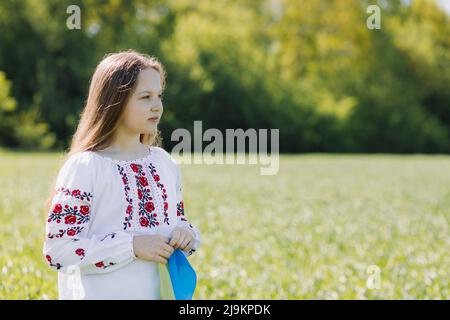 Mädchen in einem weißen bestickten Hemd mit der Nationalflagge der Ukraine in einem Weizenfeld im Frühjahr. Für Text platzieren. Hochwertige Fotos Stockfoto