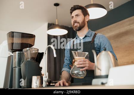 Der Barista hält in den Händen ein leeres Glasgefäß für die Zubereitung von Filterkaffee Stockfoto