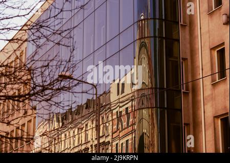 Katowice, Schlesien, Polen; März 19., 2022: Altes Mietshaus modernisiert mit einer neuen Glasfassade mit einer Reflexion der renovierten Stadthäuser Stockfoto