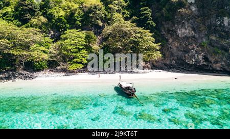 Thailändisches Longtail-Boot vor Anker an einem weißen Sandstrand auf Ko Kai (Chicken Rock Island) in Krabi Thailand mit tropischem türkisblauem Wasser und Korallenriff Stockfoto