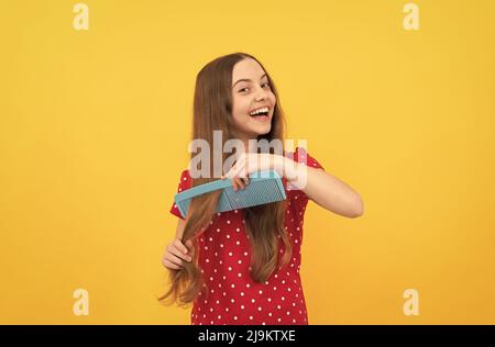 Happy Kid Kämmen lange Haare. Friseur. Mädchen hat wellige Frisur halten Haarbürste. Teen Schönheit Frisur Stockfoto