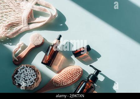 Naturkosmetik, Holzbürsten, Ohrreinigungssticks, braune Kosmetikflaschen aus Glas und Netzbeutel auf hellblauem Tisch mit harten Schatten. Kein Abfall CO Stockfoto