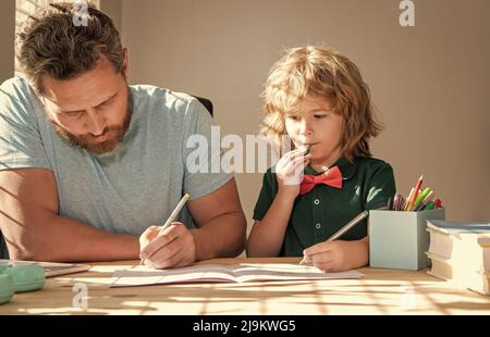 Bärtiger Vater schreibt Schulaufgaben mit seinem Jungen Sohn im Klassenzimmer, in der Schule Stockfoto