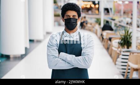 Porträt Kleinbetrieb afroamerikanischen Café-Arbeiter multirassischen Mann Restaurant Verkäufer in Schürze suchen Kamera posiert Kreuzung Arme Kellner in medizinischen Stockfoto