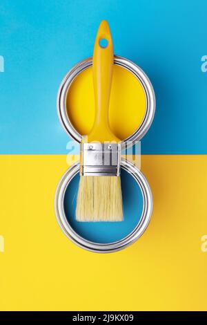 Dose mit gelber Farbe mit Pinsel auf gelbem und blauem Hintergrund. Draufsicht, Umgestaltung in ukrainischen Flaggen-Farben. Stockfoto