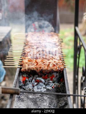 Fleischstücke, die bei Sonnenuntergang auf Metallspießen auf dem Grill aufgereiht wurden Stockfoto