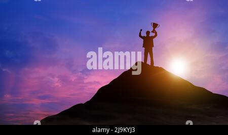 Silhouette Sieg Geschäftsmann mit Trophäe kletterte auf die Spitze des Berges über den Himmel und Sonnenlicht Hintergrund. Erfolg, Zielerreichung, Führung. Stockfoto