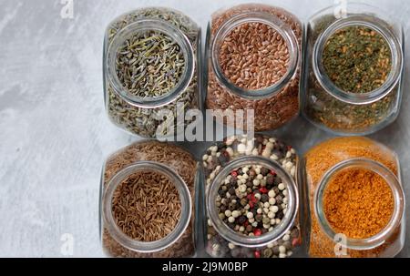 Kleine Gläser mit verschiedenen Gewürzen. Peppercorn, Kardamom, Kurkuma, Curry, Leinsamen, Kurkuma Nahaufnahme Foto. Stockfoto