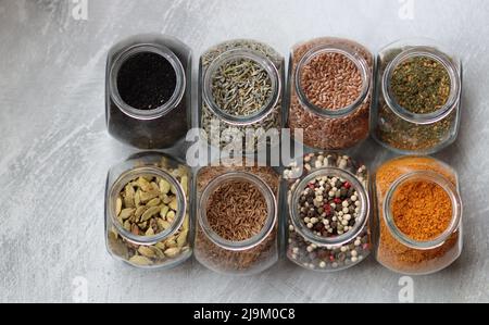 Kleine Gläser mit verschiedenen Gewürzen. Peppercorn, Kardamom, Kurkuma, Curry, Leinsamen, Kurkuma Nahaufnahme Foto. Stockfoto