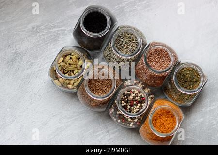 Kleine Gläser mit verschiedenen Gewürzen. Peppercorn, Kardamom, Kurkuma, Curry, Leinsamen, Kurkuma Nahaufnahme Foto. Stockfoto