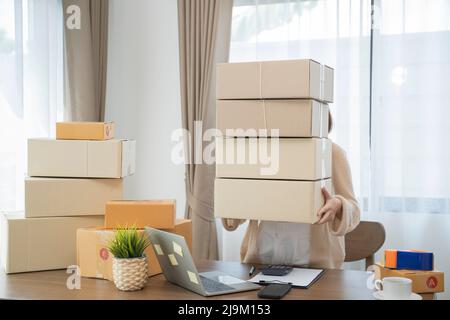 Junge asiatische Frau, die ihren Laptop benutzt und zu Hause arbeitet, Inhaberin eines kleinen Unternehmens oder Gründerin eines kleinen Unternehmens, die im Online-Marketing arbeitet Stockfoto