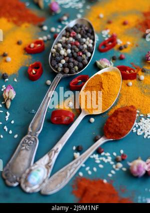 Löffel mit Gewürzen Nahaufnahme. Kurkuma, Paprikapulver, Kichererbsen, Knoblauch, Pfeffer, bay Blätter auf einem Tisch. Buntes Bild von aromatischen Gewürzen und Stockfoto