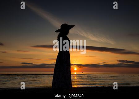 Frau in Silhouette am britischen Strand bei Sonnenuntergang. Stockfoto