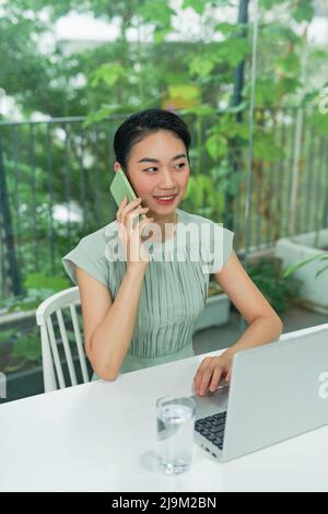 Junge asiatische Unternehmerin, die während der Arbeit im Heimbüro telefoniert. Stockfoto