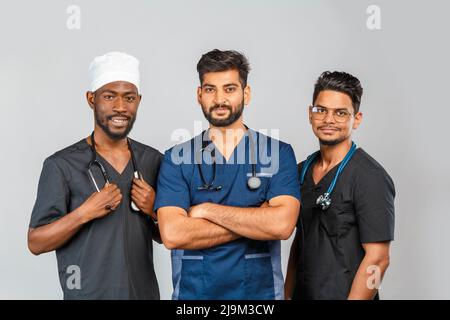 Attraktives medizinisches Team, das auf hellgrauem Hintergrund zusammensteht. Afroamerikanische Krankenschwester und zwei indische Ärzte Stockfoto