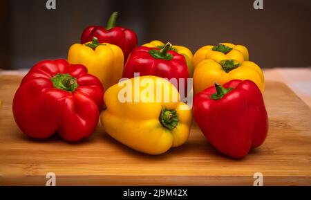 Nahaufnahme von verschiedenen roten und gelben Paprika auf einem Schneidebrett in der Küche platziert. Auch bekannt als Sweet Pepper, Pepper oder Capsicum. Stockfoto