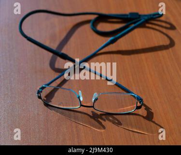 Augenbrille mit Nackenband auf einem braunen Holztisch mit selektivem Fokus. Stockfoto
