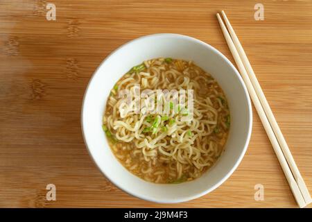 Frisch zubereitete Ramen-Nudeln in einer weißen Schüssel und auf einen Holztisch gestellt. Stockfoto