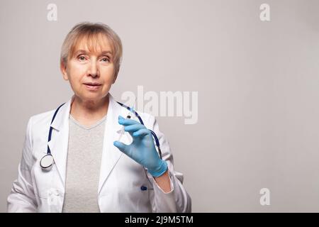 Reife Frau Arzt hält Spritze auf grauem Hintergrund Stockfoto