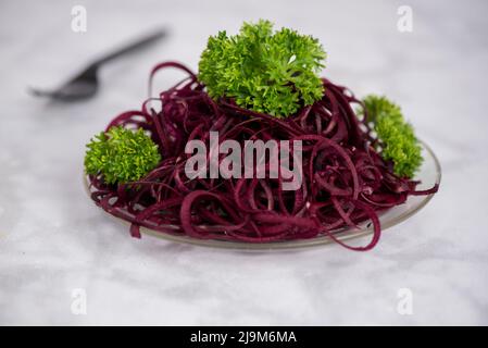 Rüsselsalat, spiralförmig, mit Petersilie auf Marmortisch und Glasplatte dekoriert, bereit zum Essen, Seitenansicht Stockfoto