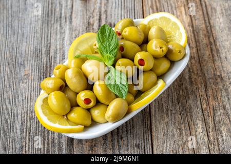 Grüne Oliven gefüllt mit Paprika. Natürliche gepfefferte Oliven auf Holzboden Hintergrund. Gesunde Ernährung. Nahaufnahme Stockfoto