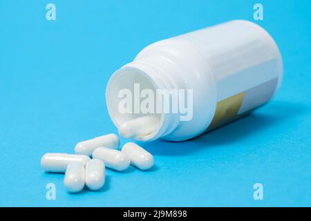 Ein Glas mit Nahrungsergänzungsmitteln und weißen Kapseln auf blauem Hintergrund. Vitamine und Spurenelemente für eine komplette Ernährung Stockfoto