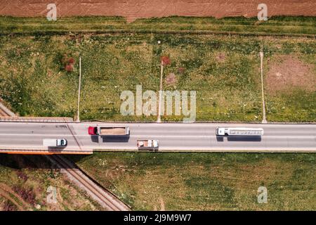 Luftaufnahme von zwei Sattelschlepper und zwei Lastkraftwagen auf der Autobahn mit Eisenbahnüberführung, direkt über Drohne pov geschossen Stockfoto