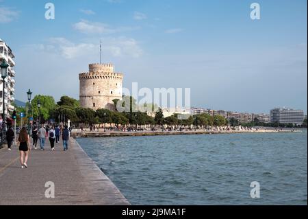 Wunderschöne Aussicht auf den weißen Turm eine berühmte Touristenattraktion in Thessaloniki, gefüllt mit geschäftigen Touristen, die an einem bewölkten Tag Masken tragen. Stockfoto