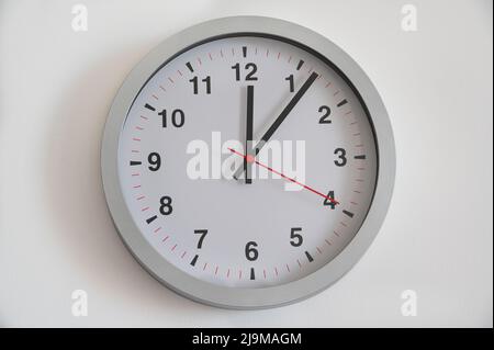 Eine moderne analoge Wanduhr, die die Zeit fünf Minuten nach zwölf in einem weißen Hintergrund anzeigt. Zeitbezogene Fotografie. Stockfoto