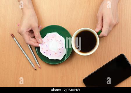 Eine Tasse Kaffee und ein bemalter Donut auf einer Untertasse. Das Konzept des Mangels an Nahrung oder Geld Stockfoto