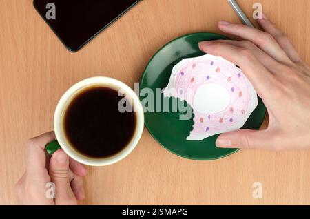 Eine Tasse Kaffee und ein bemalter Donut auf einer Untertasse. Das Konzept des Mangels an Nahrung oder Geld Stockfoto