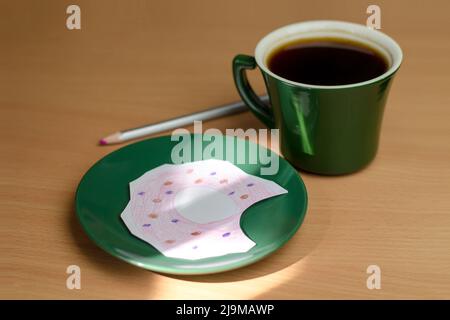 Eine Tasse Kaffee und ein bemalter Donut auf einer Untertasse. Das Konzept des Mangels an Nahrung oder Geld Stockfoto