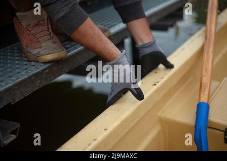 Der Typ schiebt das Boot vom Dock weg. Details zur Bootstation. Der Mann hält mit den Händen Seite des Bootes. Details der Anlegestelle. Stockfoto