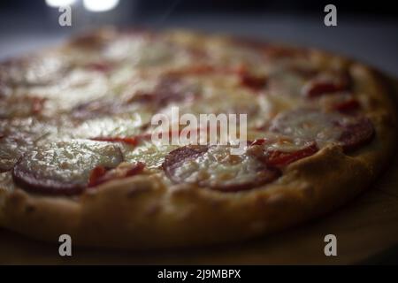 Pizza an der Theke. Essen mit Käse und Wurst. Gebratene Pizza in der Küche. Gebackene Lebensmittel mit hohem Fettgehalt. Stockfoto